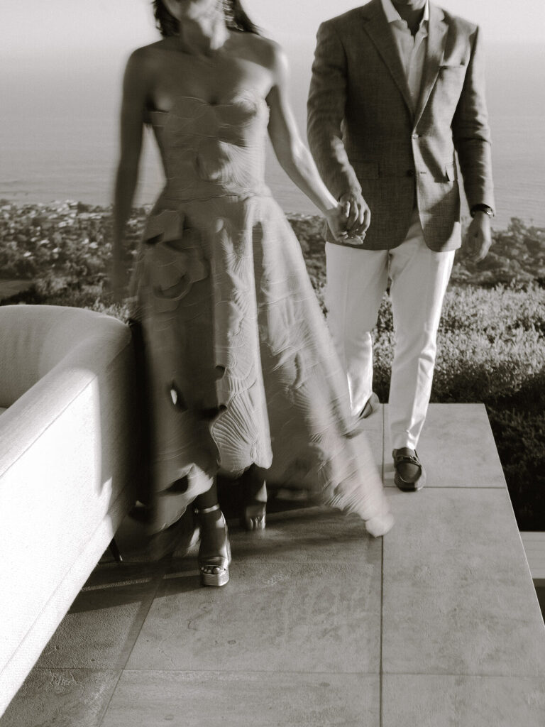 A warm monochrome frame of the couple walking hand in hand along the terrace