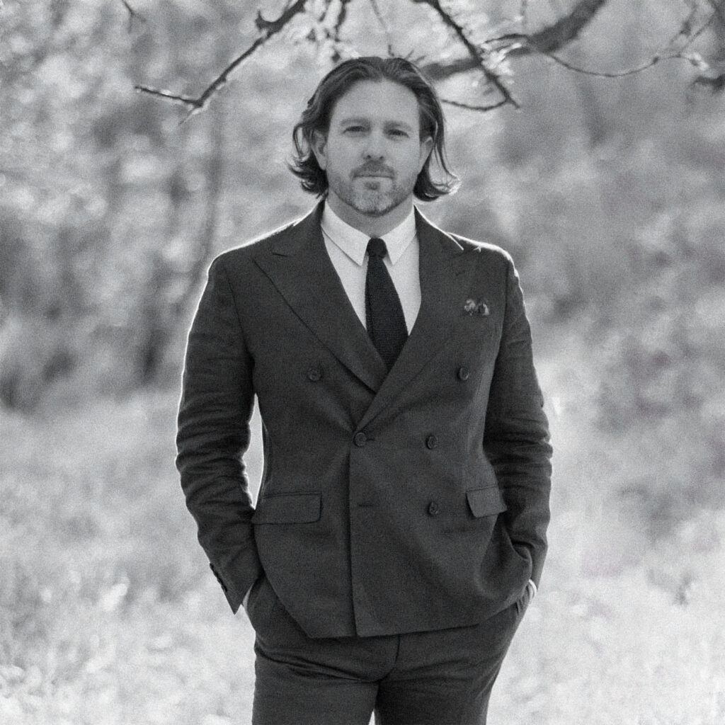 Paul Von Rieter in a double breasted suit and knit tie, photographed in black and white