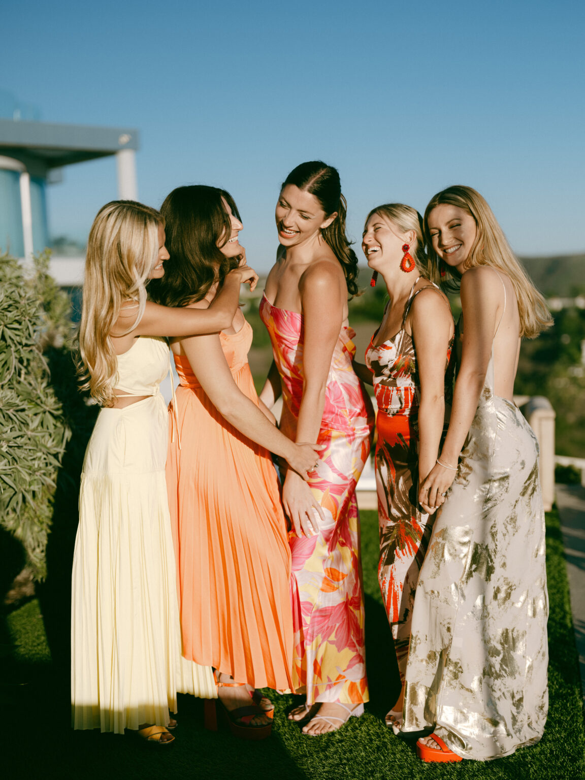 Five women in citrus toned silk laughing together on a terrace