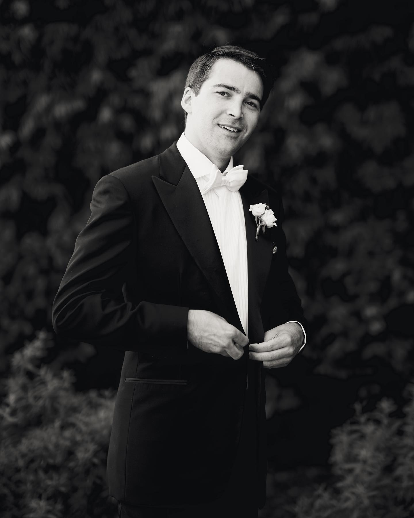 A monochrome portrait of the groom in white tie, fastening his jacket before the ceremony