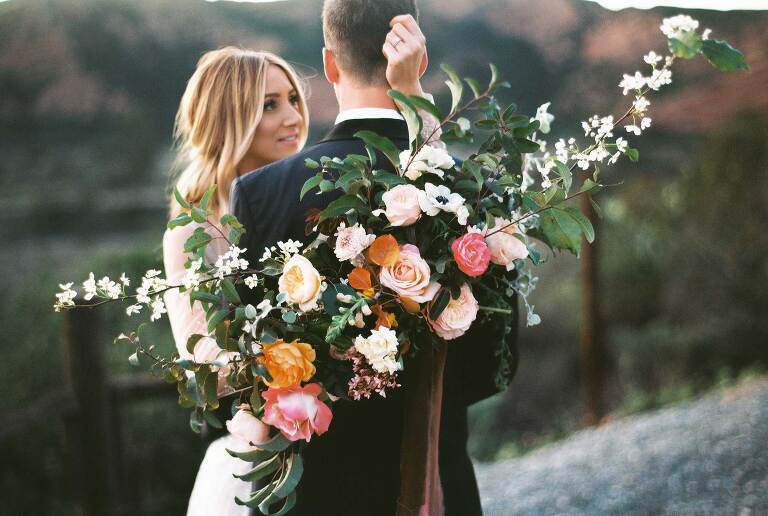 The couple close together on the hillside, peach garden roses filling the foreground