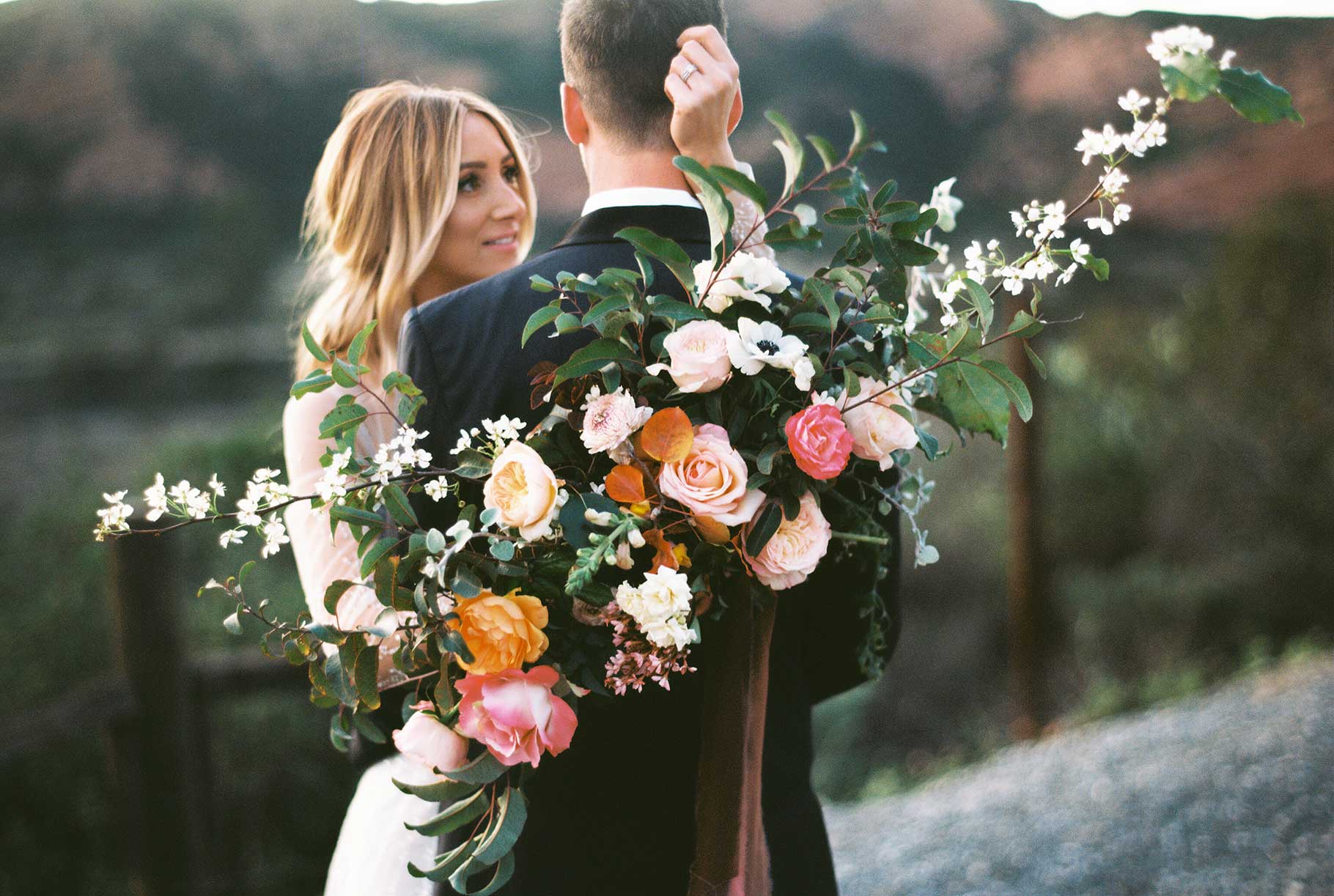 The couple close together on the hillside, peach garden roses filling the foreground